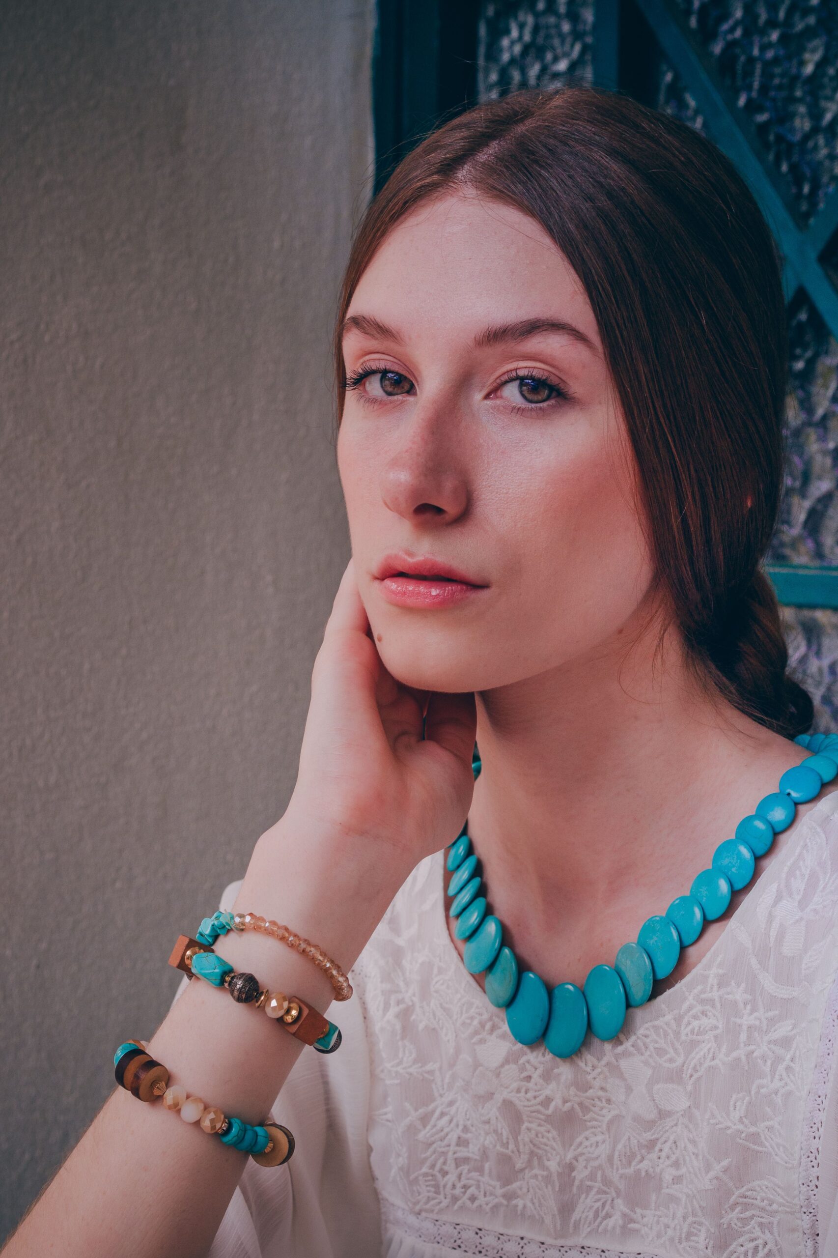 Stylish woman with turquoise necklace and bracelets, posing indoors.